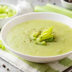 Zuppa cremosa di sedano verde, guarnita con gambi freschi e pepe nero. Accanto, una ciotola di sedano a cubetti.