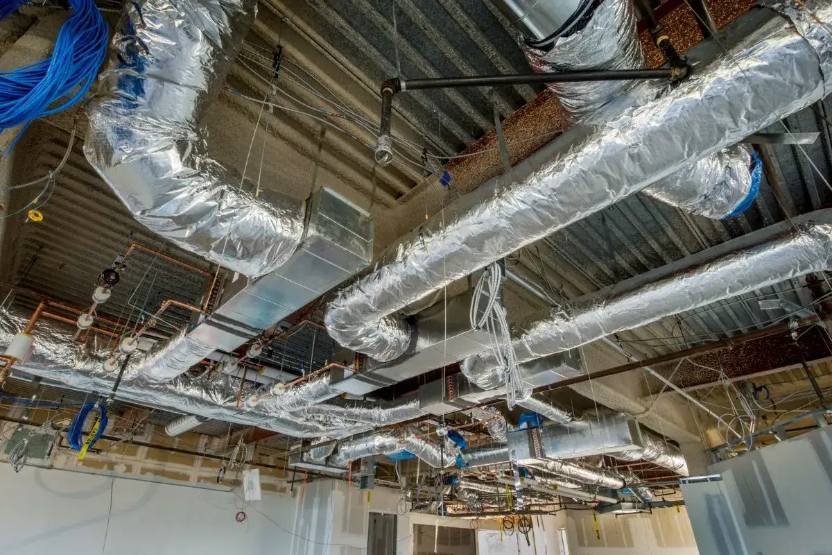 Soffitto con condotti isolati, cavi blu e tubi di rame. Si intravedono i primi elementi di aspiratori elicoidali in fase di installazione.